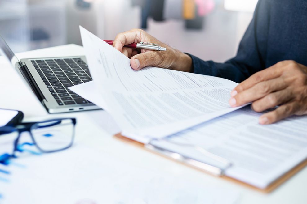 Person mit Dokumenten und Laptop